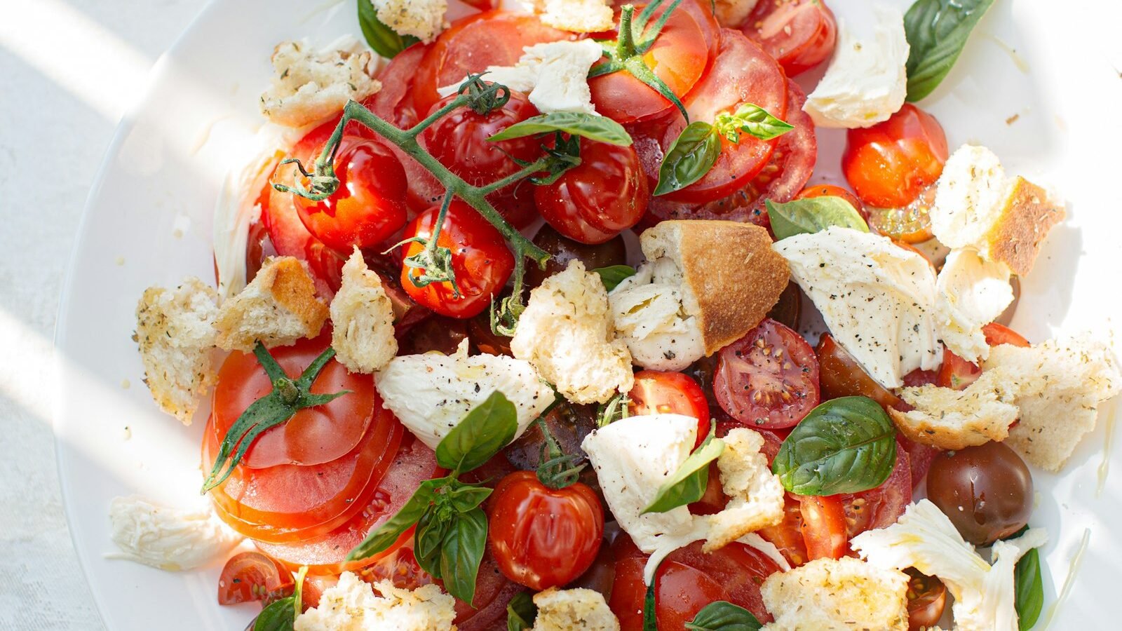 Caprese salade met burrata, rijpe tomaten, verse basilicum en groene pesto op een wit bord
