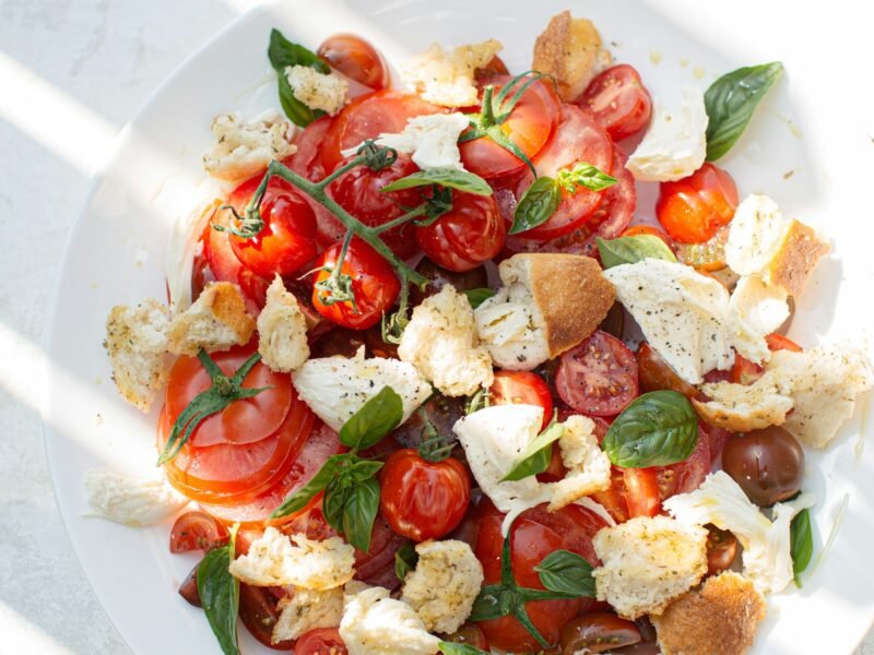Caprese salade met burrata, rijpe tomaten, verse basilicum en groene pesto op een wit bord