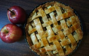 Klassieke appeltaart met deegruitjes en een verse appel ernaast