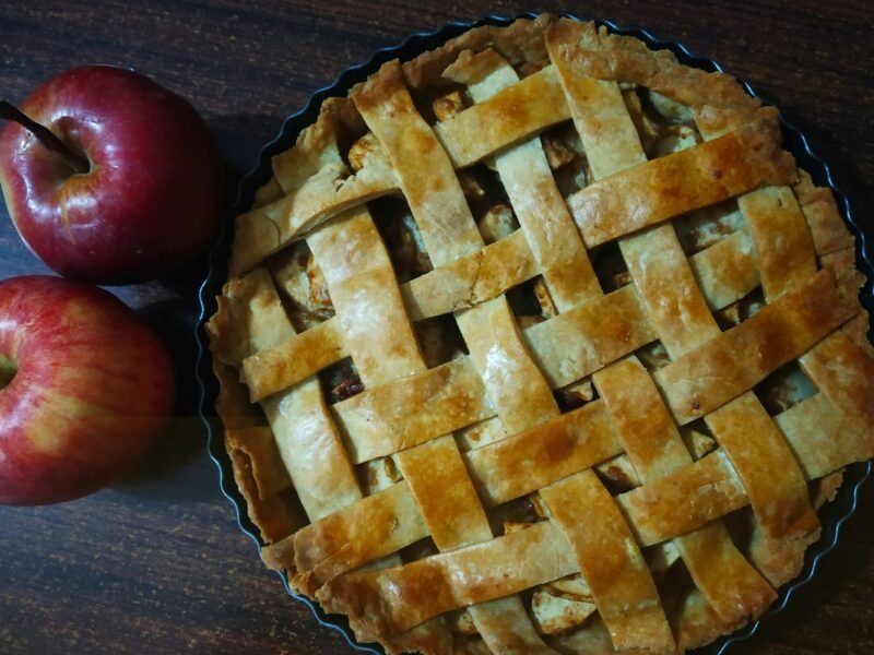 Klassieke appeltaart met deegruitjes en een verse appel ernaast