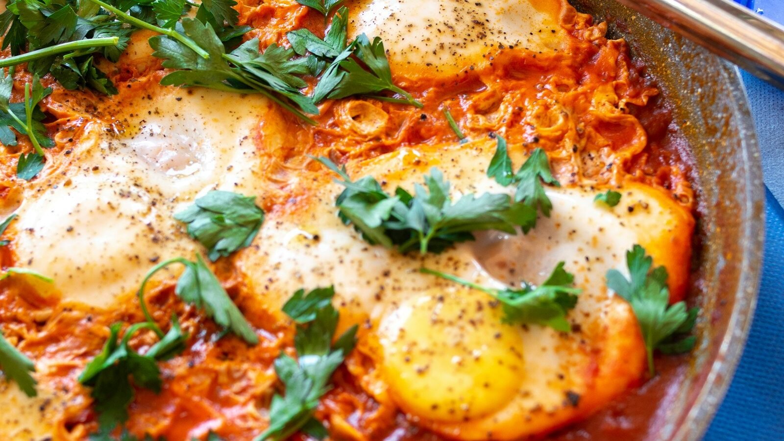 Shakshuka met zachtgekookte eieren in pittige tomatensaus, verkruimelde feta en verse kruiden in een gietijzeren pan