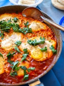 Shakshuka met zachtgekookte eieren in pittige tomatensaus, verkruimelde feta en verse kruiden in een gietijzeren pan