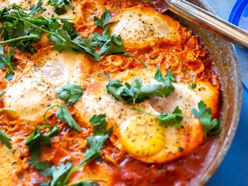 Shakshuka met zachtgekookte eieren in pittige tomatensaus, verkruimelde feta en verse kruiden in een gietijzeren pan